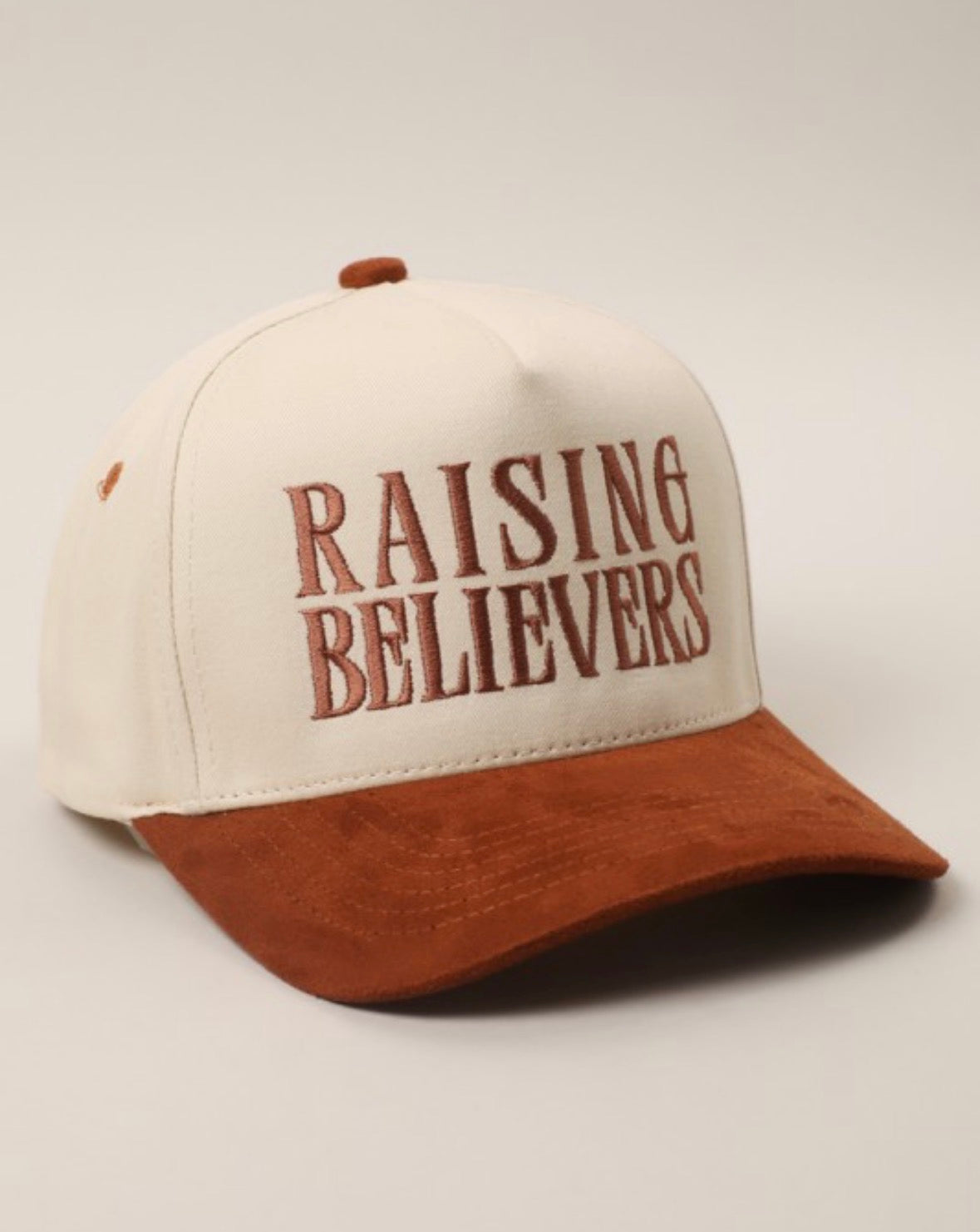 Cap with 'RAISING BELIEVERS' text on a beige background