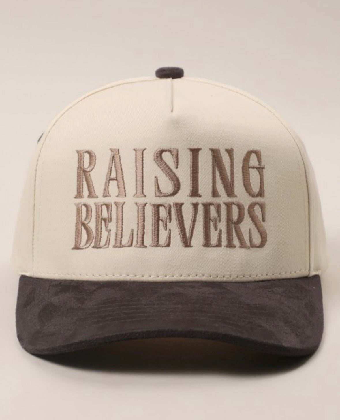 Beige and brown cap with 'RAISING BELIEVERS' text on a light gray background